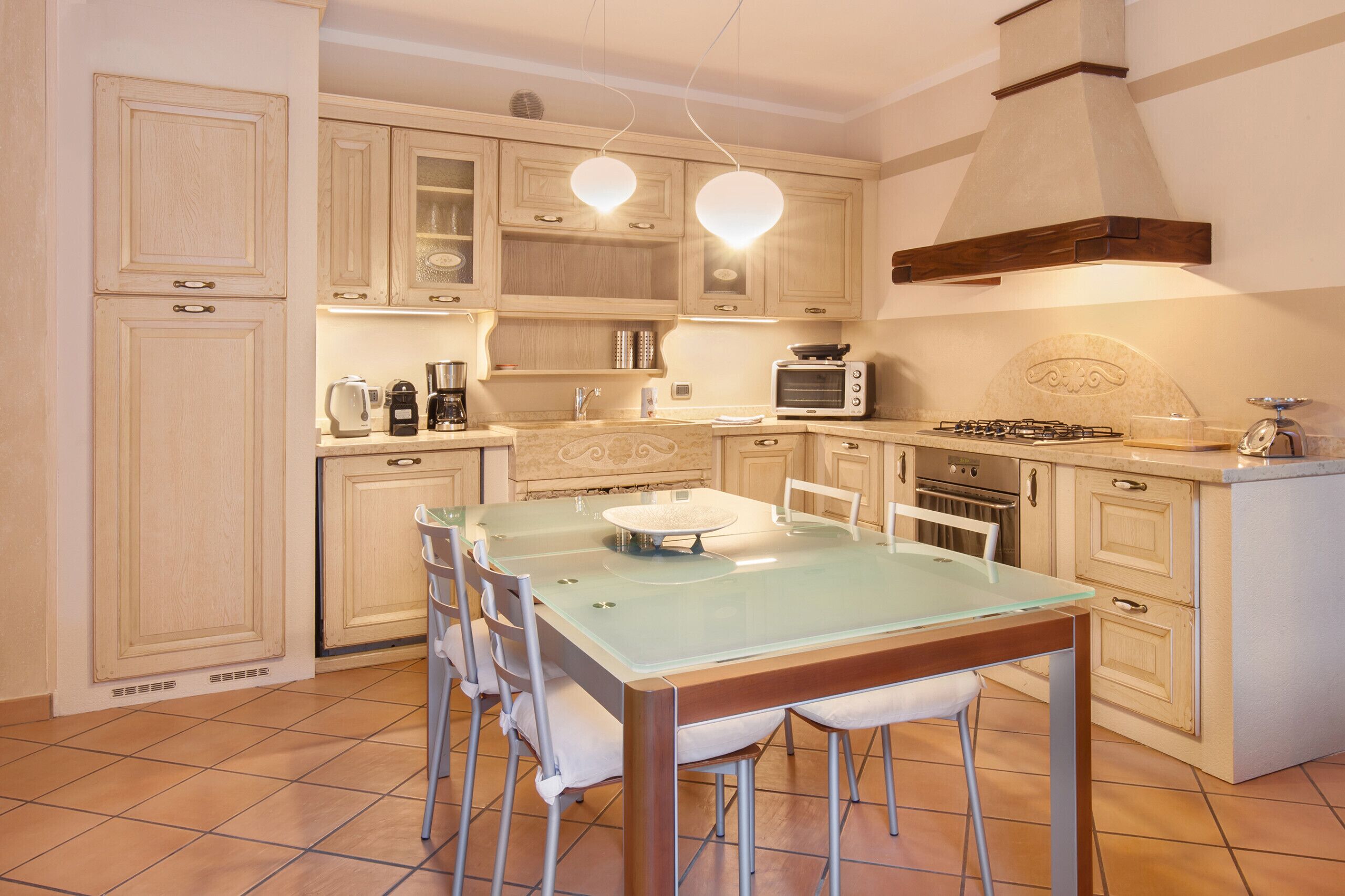 Una cocina con armarios de madera clara, una mesa de comedor con superficie de vidrio y electrodomésticos modernos, incluyendo un microondas y una estufa.
