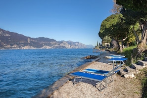 A lakeside view with a row of blue lounge chairs along the shore, surrounded by rocky terrain and trees.