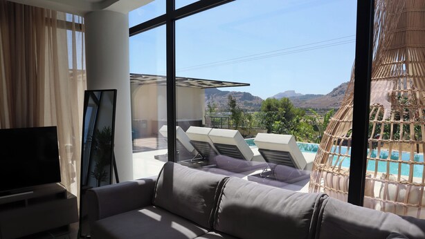 Ein modernes Wohnzimmer mit Sofa, Flachbildfernseher und Blick auf Pool und Berge.
