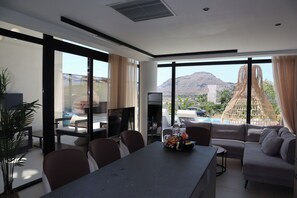 A modern hotel room with a dining area, a sofa, and large windows offering a mountain view.