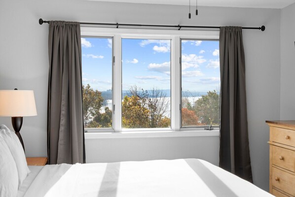 A bedroom with a bed, a nightstand, a dresser, and a window with curtains.