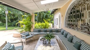 A covered outdoor seating area with a curved sofa, a coffee table, and a potted plant.