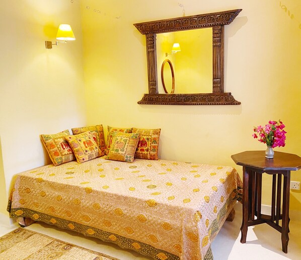 A bedroom with a bed, pillows, a nightstand, a mirror, and a vase with flowers.