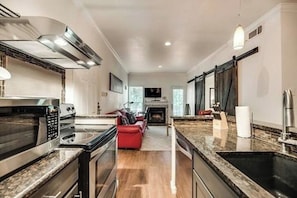 A modern kitchen with a microwave, stove, and sink. There is a red sofa in the living area and a fireplace. - I50 - Apt|Patio|11mi to Convention Ctr|Sleeps 2 (Irving)