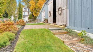 A rustic barn with a large open door, surrounded by a well-maintained garden and a brick pathway leading to the entrance.