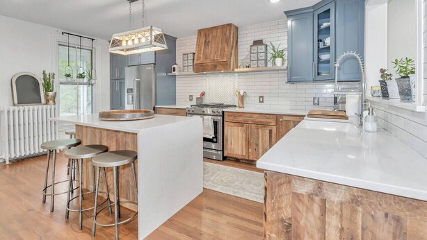 A modern kitchen with a central island, bar stools, wooden cabinets, and a large window.
