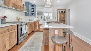 A modern kitchen with wooden cabinets, a large island with stools, a built-in oven, and a hanging light fixture.