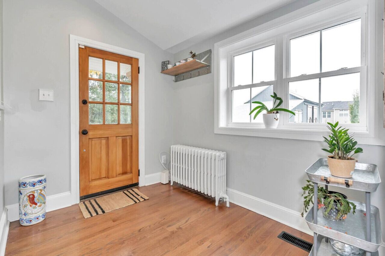 A clean, well-lit entryway with a wooden door, a white radiator, and a window with a view of houses.