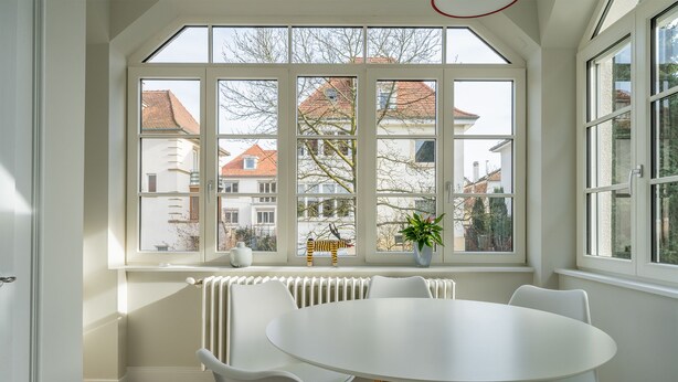 Ein Zimmer mit einem großen Fenster, einem weißen Tisch und weißen Stühlen.