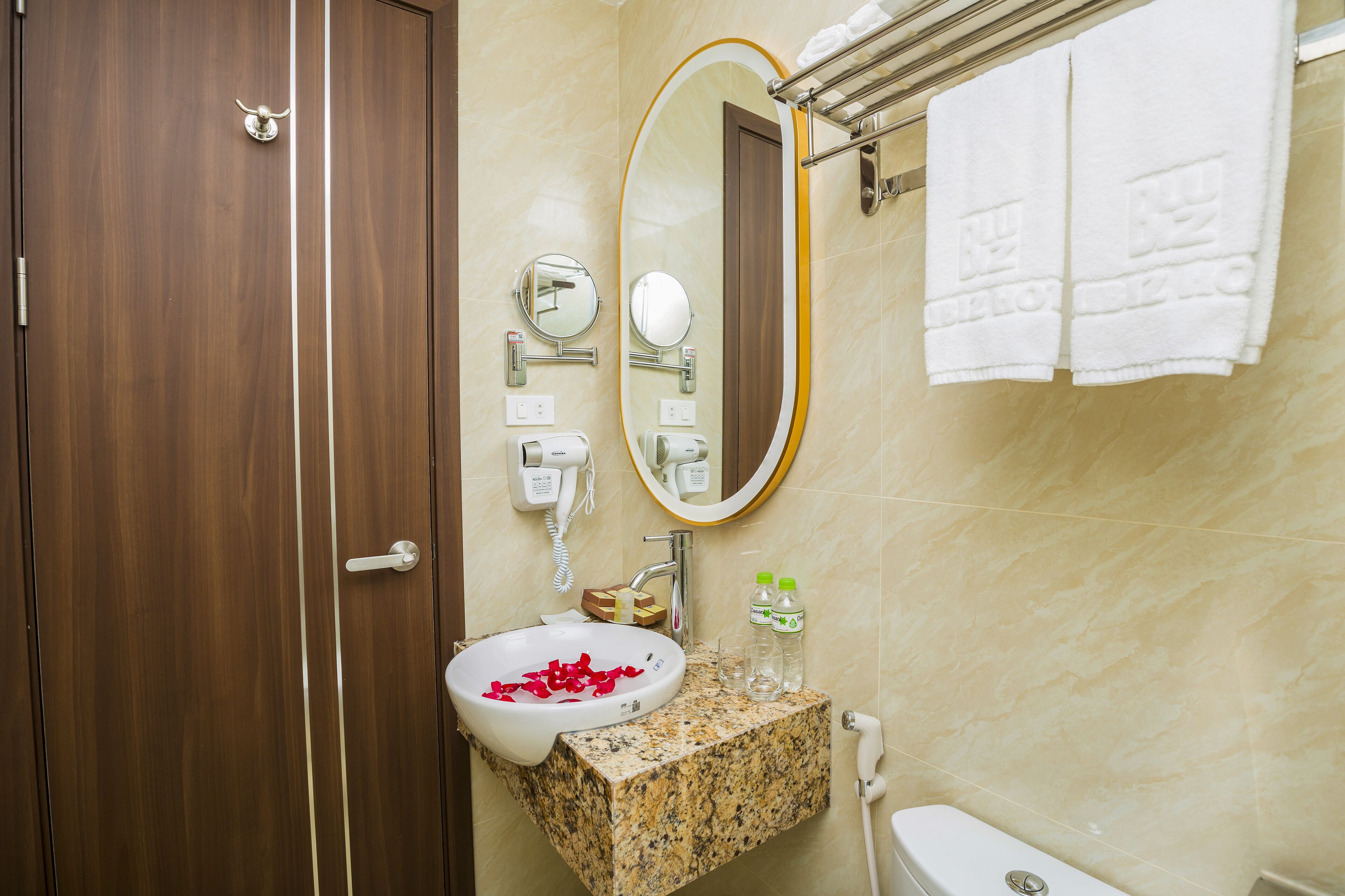 A bathroom with a wooden door, a marble sink, a mirror, a towel rack, and a toilet.