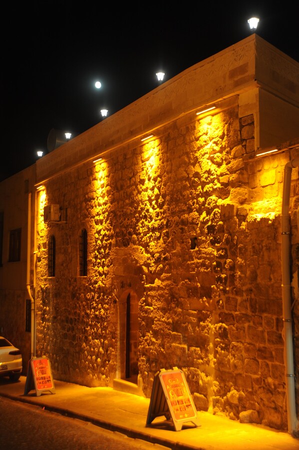 A stone building with illuminated windows and a signboard on the ground. - Artukhan Konak (Mardin)