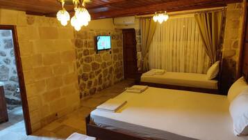 Una habitación con pared de piedra, techo de madera, cama con cabecera, televisor y ventana con cortinas.