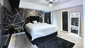 Een moderne slaapkamer met een bed, nachtkastje en een grote spiegel.