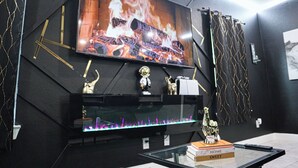 Een kamer met een televisie waarop een haard te zien is, een trofee op een plank en een glazen tafel met een boek en een afstandsbediening.