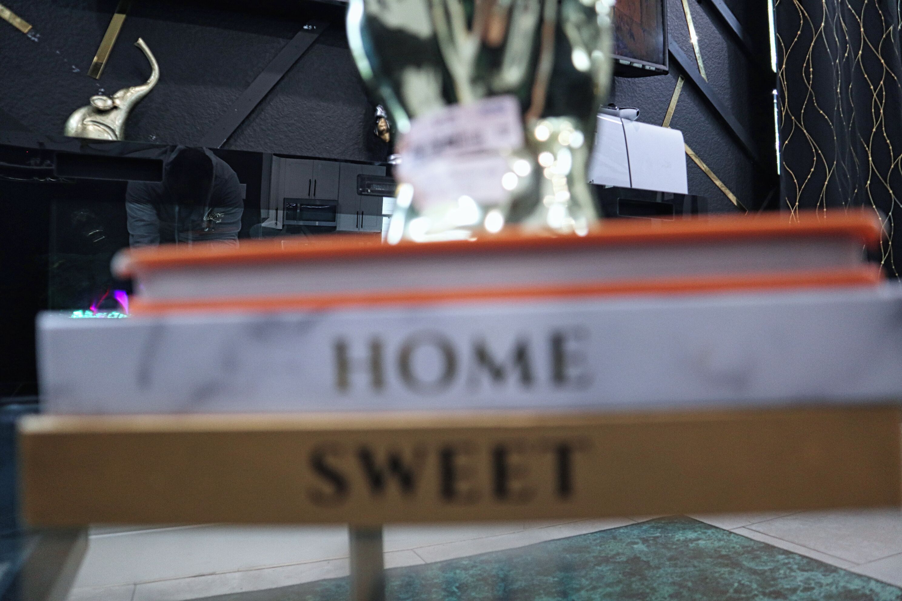 A sign with the words 'HOME SWEET' and a blurred background with a trophy.