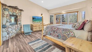 Une chambre avec un mur en pierre, un lit avec une literie à motifs, un banc en bois, une chaise bleue et une commode.