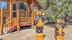 Une cabane en rondins avec un porche et deux statues d’ours portant des panneaux indiquant « BIENVENUE ».