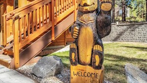 A wooden bear sculpture with the word "WELCOME" on a post, a wooden staircase, and a stone wall in the background.