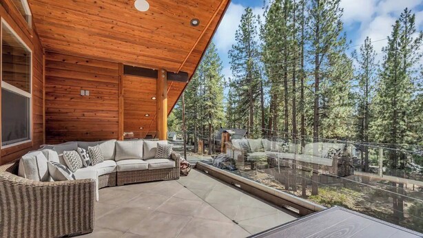 A wooden deck with a sofa and a glass table, overlooking a forested area.