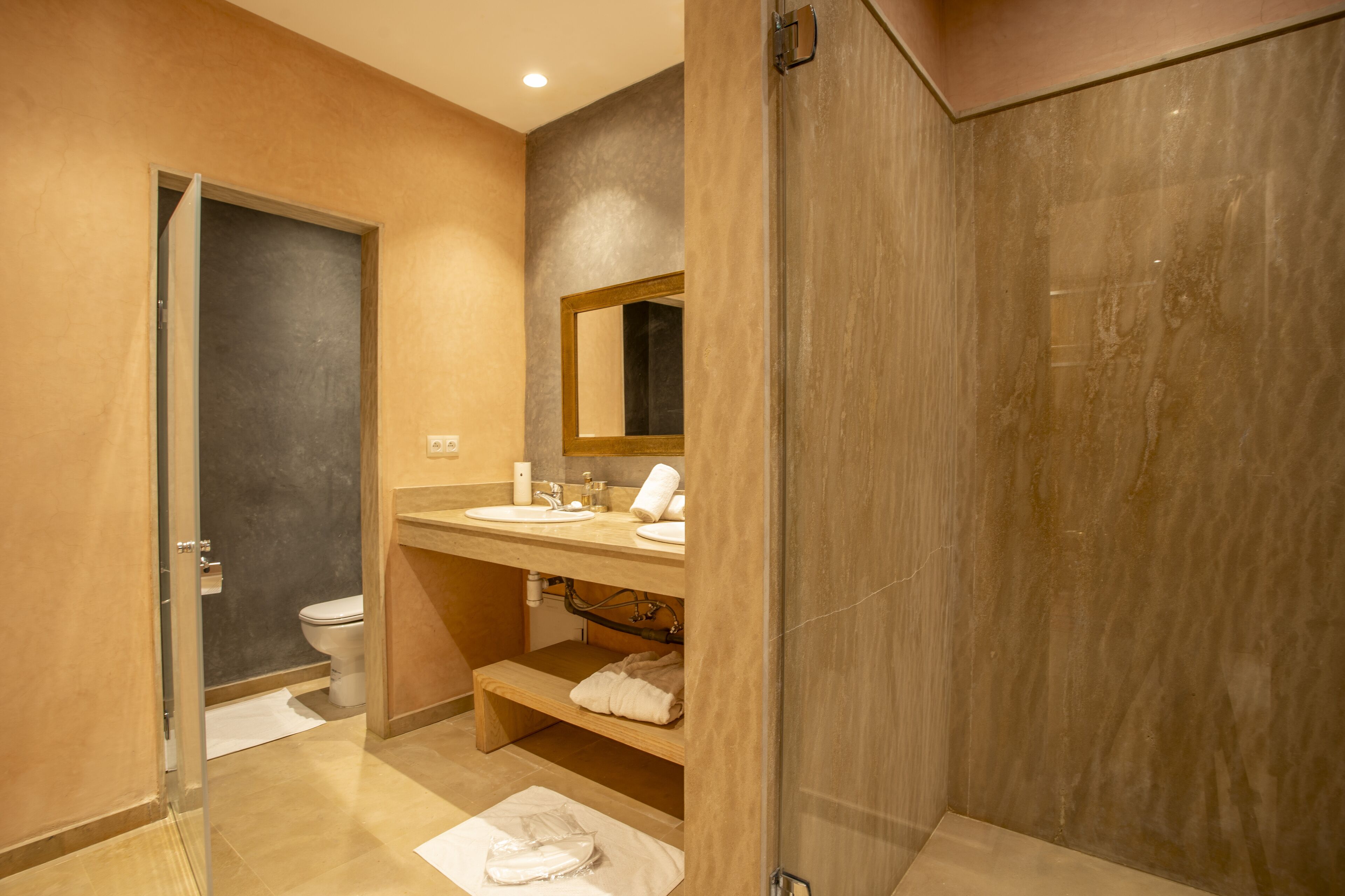Een moderne badkamer met een glazen douchecabine, een houten wastafelmeubel en een toilet.