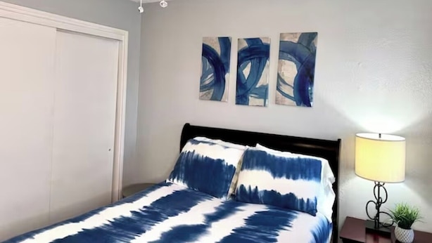 Une chambre à coucher avec un lit, un ventilateur de plafond, une table de chevet avec une lampe et des œuvres d’art abstraites accrochées au mur.