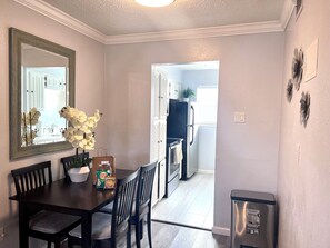 Un coin repas avec une table en bois foncé, deux chaises, un vase avec des fleurs blanches et un miroir au mur.