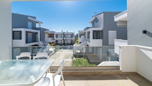 Un balcon moderne donnant sur l’extérieur, avec une table et des chaises en verre, et offrant une vue sur un quartier résidentiel avec des bâtiments contemporains.