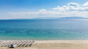 Une plage bordée de rangées de parasols et de chaises longues, un ciel dégagé et une mer calme.