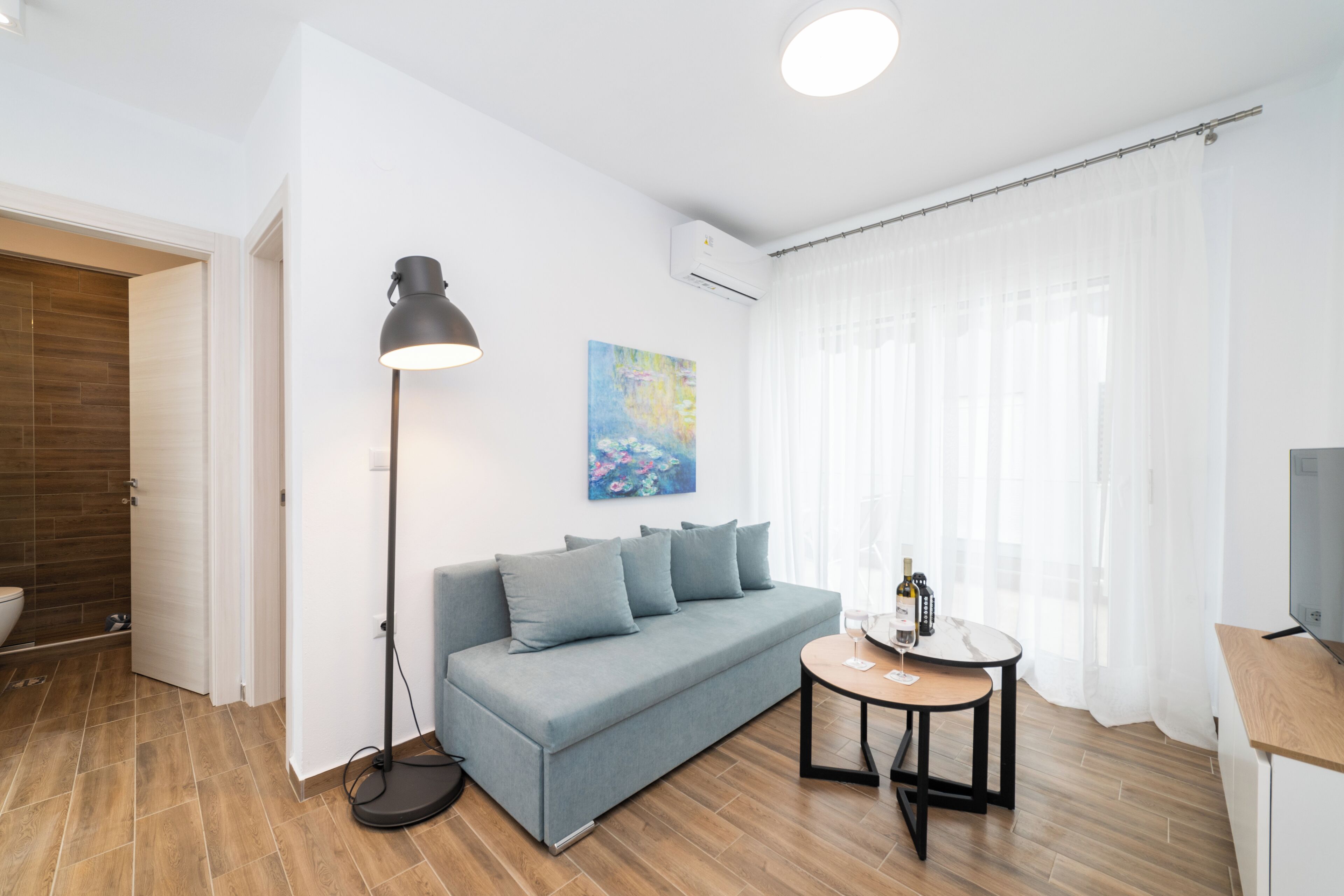 A modern living room with a sofa, a floor lamp, a small table with a wine bottle, and a painting on the wall.