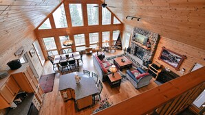 A spacious cabin interior with a high ceiling, large windows, a fireplace, and a cozy seating area. - Twin Pines: Dog-Friendly Lakefront Cabin w/ Private Dock & Kayaks (Stone Lake)