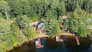 Un chalet au bord du lac, avec un accès à un quai, entouré d’une forêt dense.