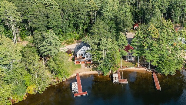 Una cabaña junto al lago con acceso a un muelle, rodeada de un bosque denso.