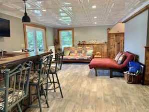 Une pièce spacieuse avec un bar en bois, un canapé confortable et un coin repas avec des chaises en métal.