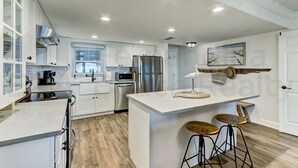A modern kitchen with white cabinetry, stainless steel appliances, and a wooden floor. - 202 Atlantis 2 Bedroom Condo by RedAwning (Fernandina Beach)