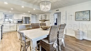A modern kitchen with white cabinetry, a dining table with wicker chairs, and a chandelier. - 202 Atlantis 2 Bedroom Condo by RedAwning (Fernandina Beach)