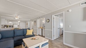 Et moderne køkken med hvide skabe, et spiseområde med en blå sofa og et lille bord, samt en gang der fører til et andet rum.