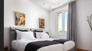 Un dormitorio moderno con una cama grande, dos cuadros en la pared y una ventana con cortinas.