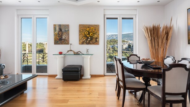 Un comedor con mesa de madera, sillas y vistas al exterior a través de amplios ventanales.