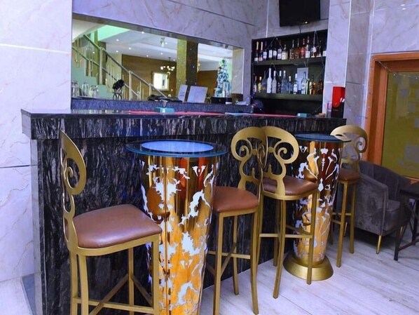Zona bar con un bancone in marmo, sedie dorate con rivestimenti decorati e una parete a specchio che riflette l'ambiente interno.