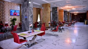 A modern hotel lobby with marble columns, red chairs, and a TV displaying a news broadcast. - The Dover Hotel Ikeja  (Lagos)