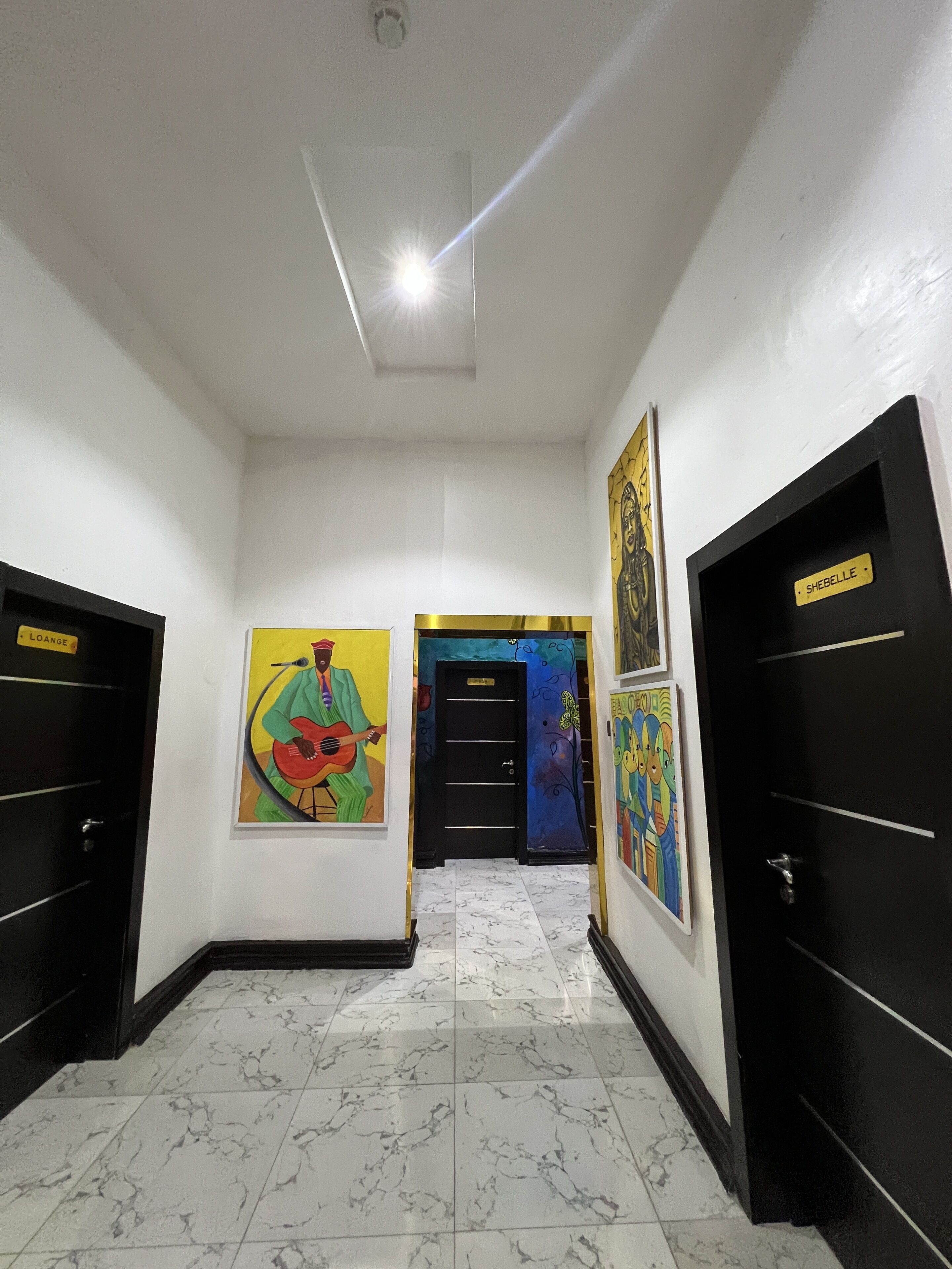 Un pasillo con puertas negras, piso de mármol y obras de arte coloridas en las paredes.
