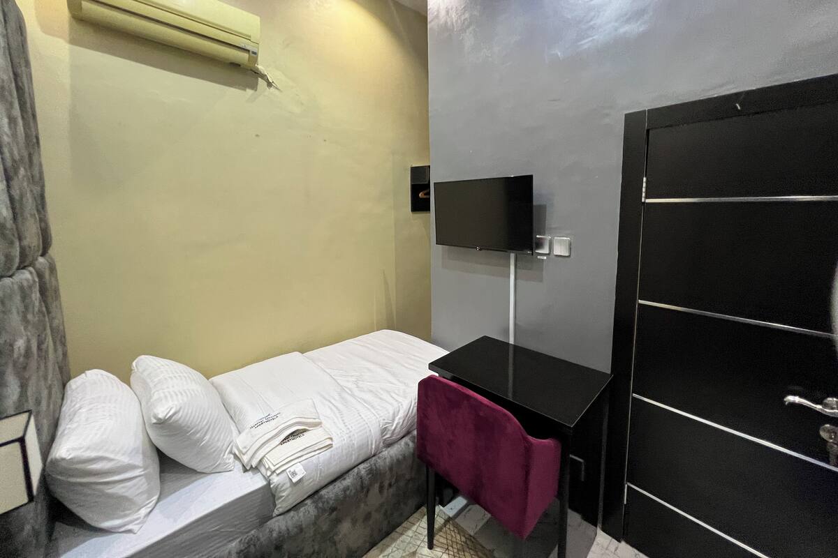 Una habitación pequeña con cama, escritorio, televisor y armario.