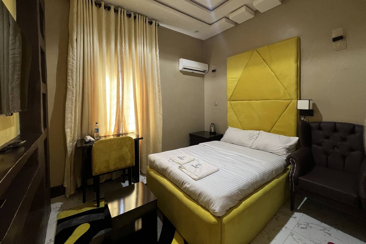 Una habitación de hotel con cama, escritorio, silla, sofá y aire acondicionado.