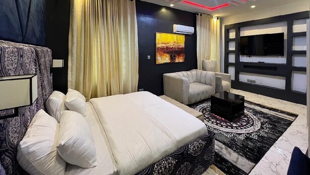 Una habitación de hotel moderna con cama, sofá, una mesa de centro y una pantalla de televisión grande.