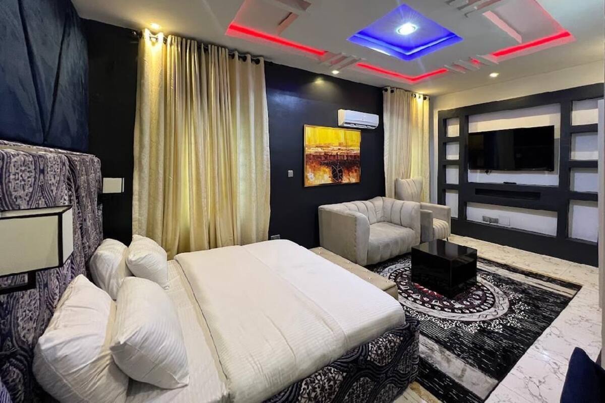 Una habitación de hotel moderna con cama, sofá, una mesa de centro y una pantalla de televisión grande.