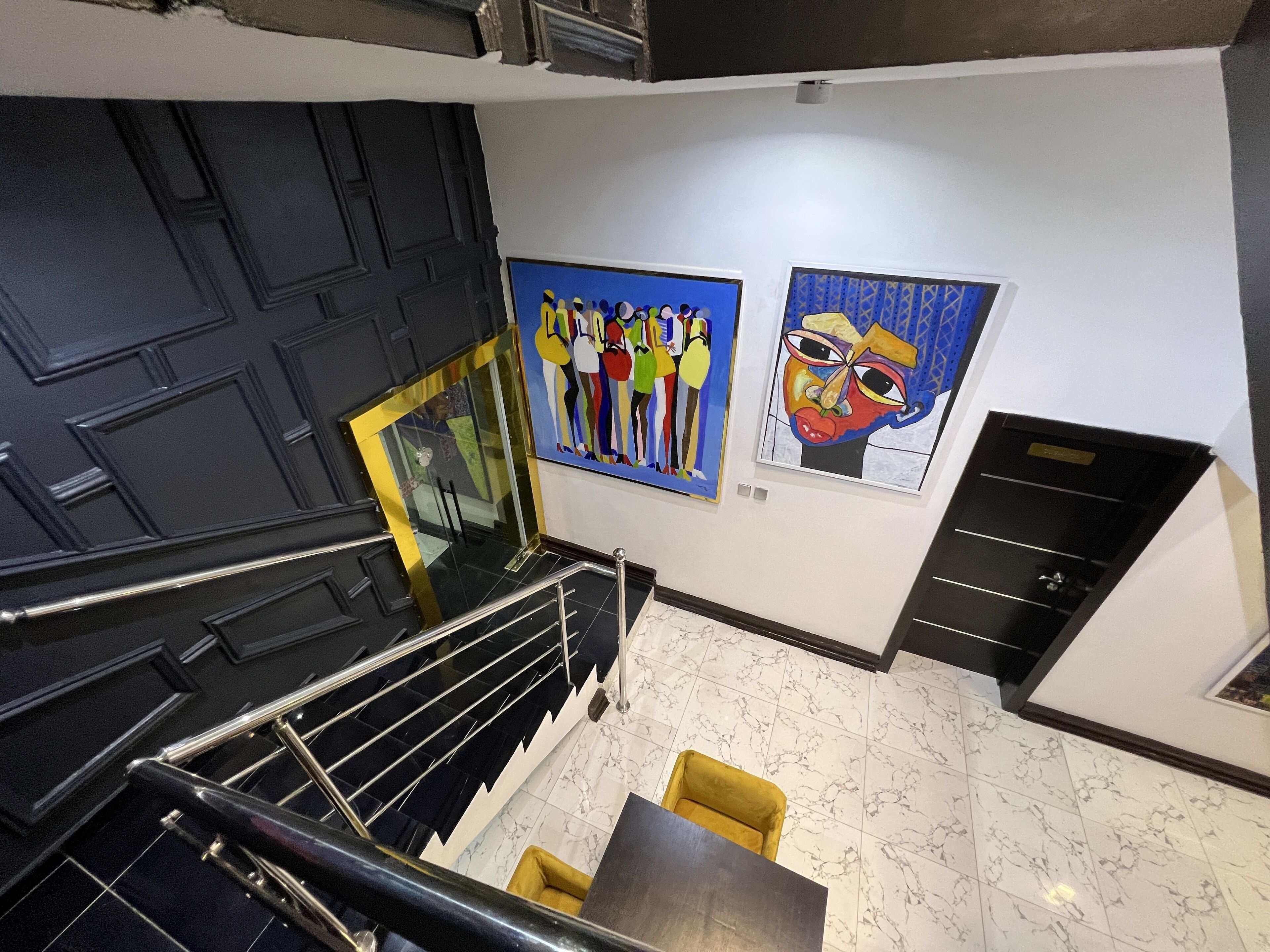 A hotel lobby with a staircase, a yellow chair, and two artworks on the wall.