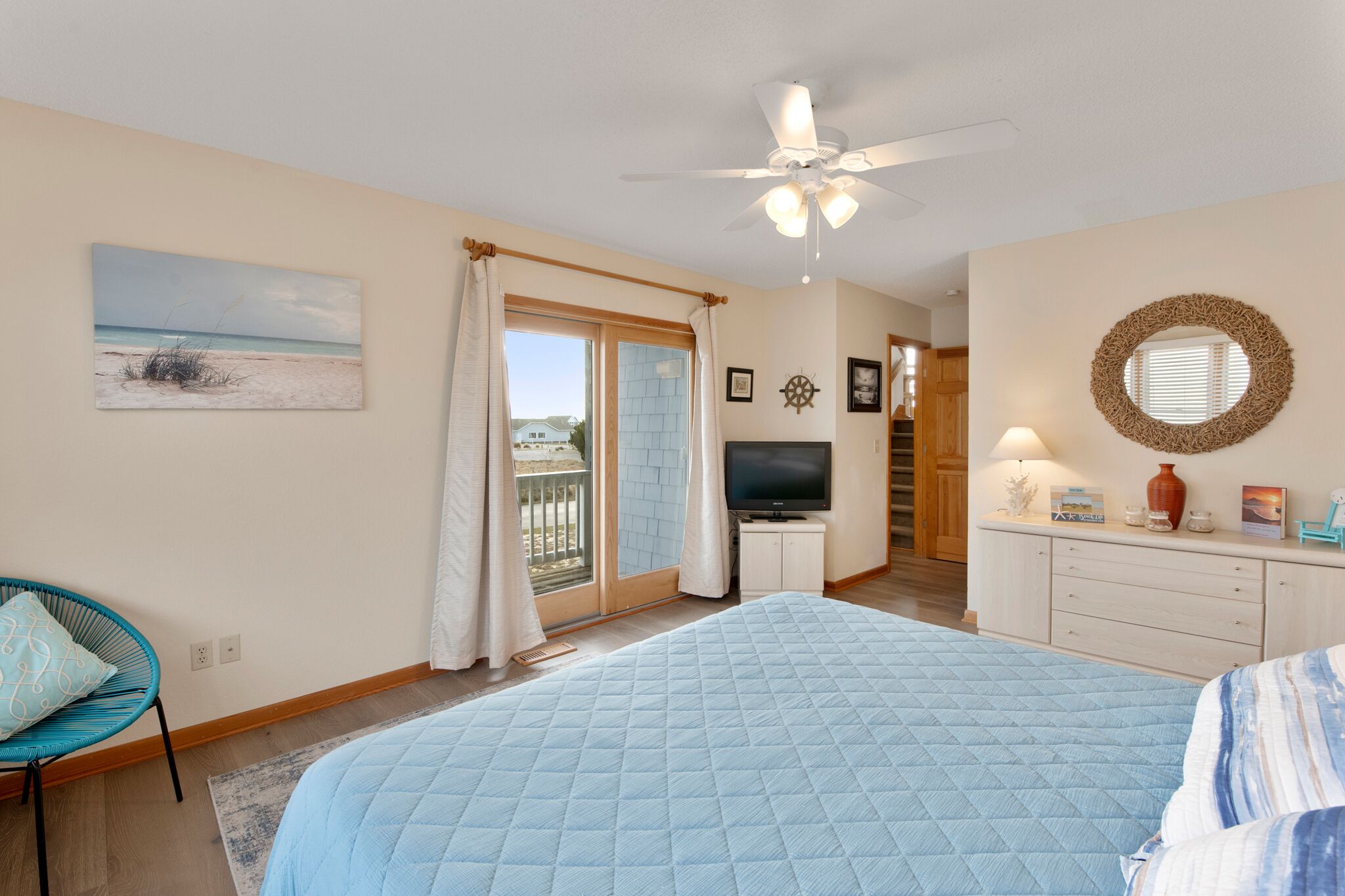 A bedroom with a large bed, a ceiling fan, a TV, and a view of the outside.