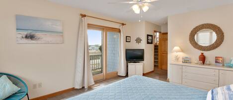 A bedroom with a large bed, a ceiling fan, a TV, and a view of the outside.