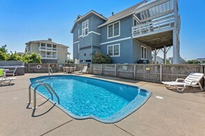 A swimming pool with a metal ladder, surrounded by a wooden fence and lounge chairs.