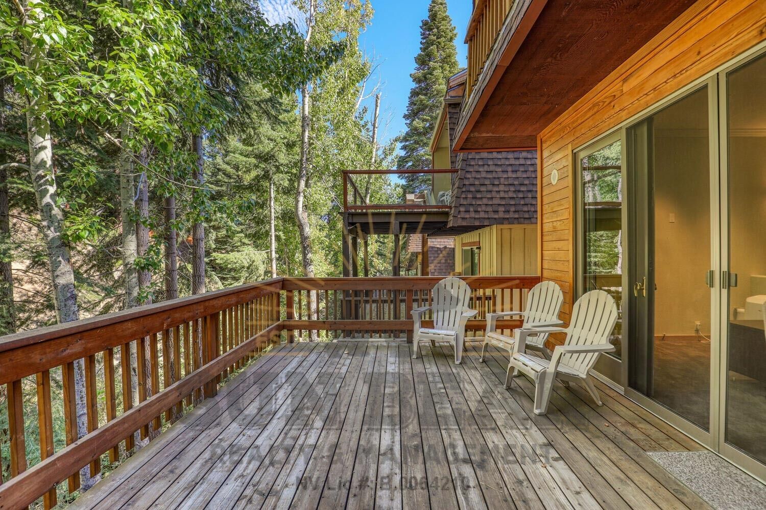 A wooden deck with Adirondack chairs, surrounded by trees.